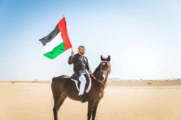 Middle eastern handsome man with typical emirates dress riding a arabic horse in the Dubai desert