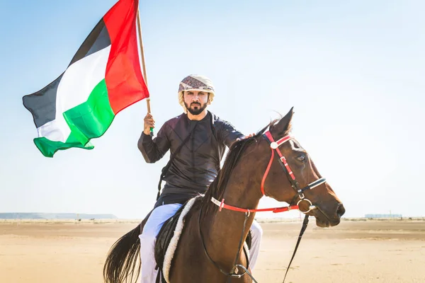 Middle eastern handsome man with typical emirates dress riding a arabic horse in the Dubai desert