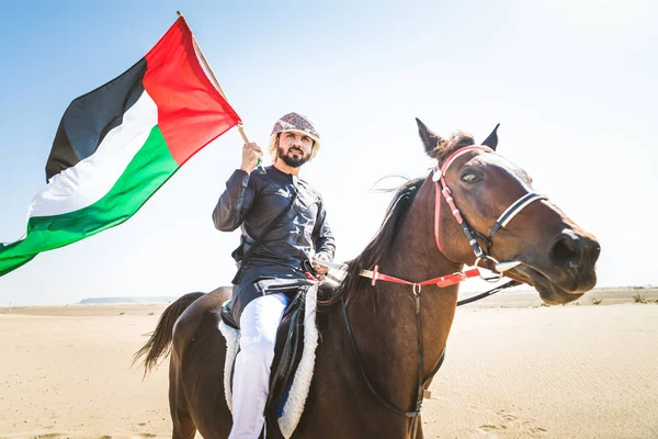 Middle eastern handsome man with typical emirates dress riding a arabic horse in the Dubai desert