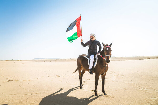 Middle eastern handsome man with typical emirates dress riding a arabic horse in the Dubai desert