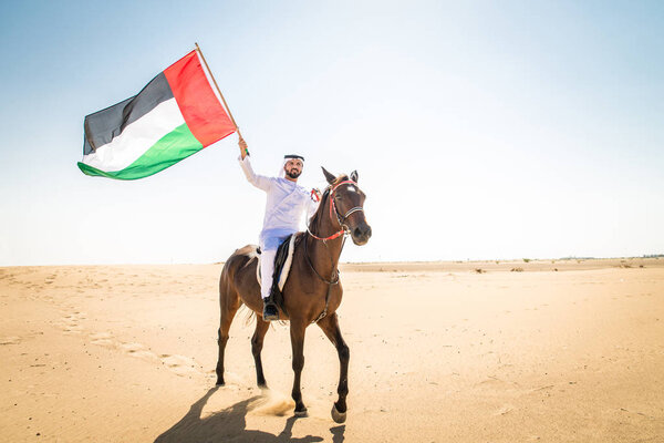 Middle eastern handsome man with typical emirates dress riding a arabic horse in the Dubai desert