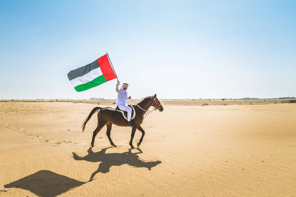 Middle eastern handsome man with typical emirates dress riding a arabic horse in the Dubai desert