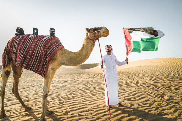 Handsome middle eastern man with kandura and gatra riding on a camel in the desert