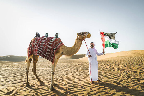 Handsome middle eastern man with kandura and gatra riding on a camel in the desert