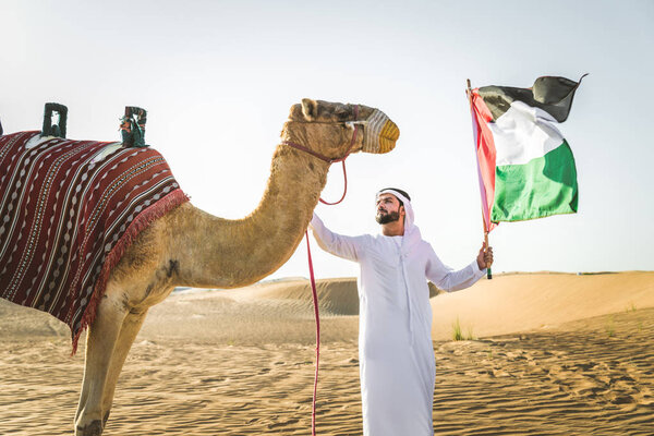 Handsome middle eastern man with kandura and gatra riding on a camel in the desert