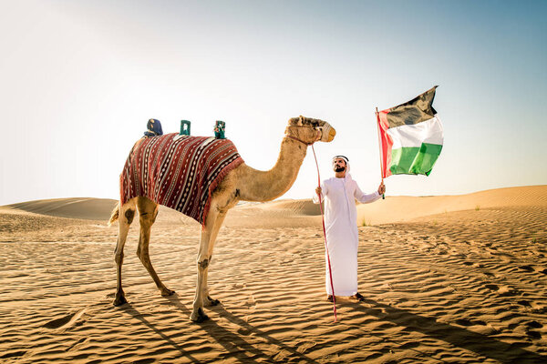 Handsome middle eastern man with kandura and gatra riding on a camel in the desert