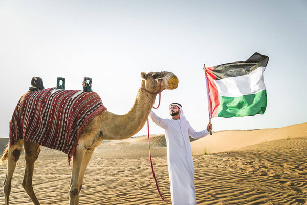 Handsome middle eastern man with kandura and gatra riding on a camel in the desert
