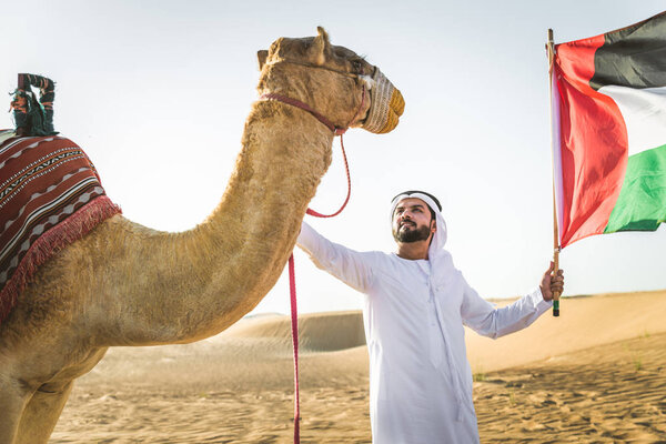 Handsome middle eastern man with kandura and gatra riding on a camel in the desert