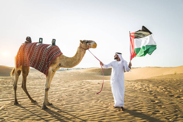 Handsome middle eastern man with kandura and gatra riding on a camel in the desert
