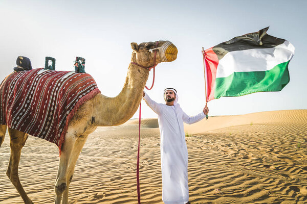 Handsome middle eastern man with kandura and gatra riding on a camel in the desert
