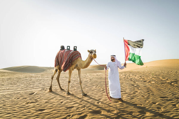 Handsome middle eastern man with kandura and gatra riding on a camel in the desert