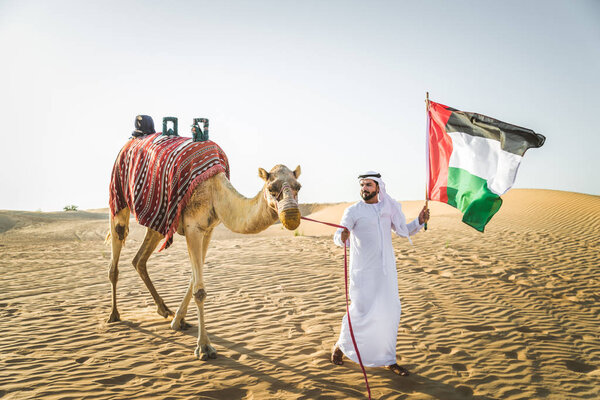 Handsome middle eastern man with kandura and gatra riding on a camel in the desert