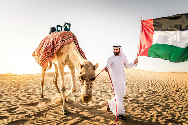 Handsome middle eastern man with kandura and gatra riding on a camel in the desert