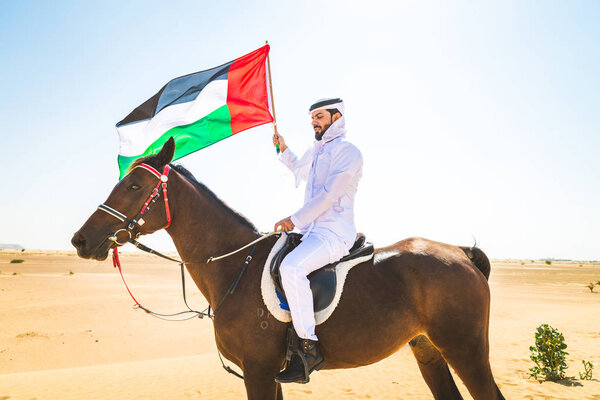 Middle eastern handsome man with typical emirates dress riding a arabic horse in the Dubai desert