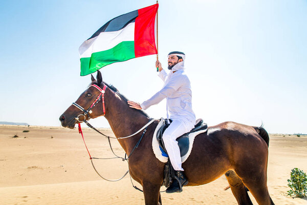 Middle eastern handsome man with typical emirates dress riding a arabic horse in the Dubai desert