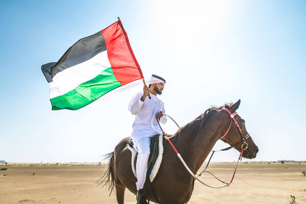 Middle eastern handsome man with typical emirates dress riding a arabic horse in the Dubai desert