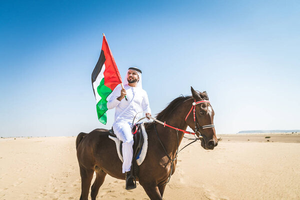 Middle eastern handsome man with typical emirates dress riding a arabic horse in the Dubai desert
