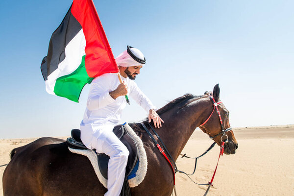 Middle eastern handsome man with typical emirates dress riding a arabic horse in the Dubai desert