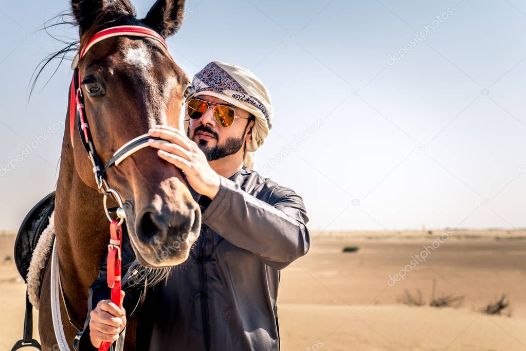 Middle eastern handsome man with typical emirates dress riding a arabic horse in the Dubai desert