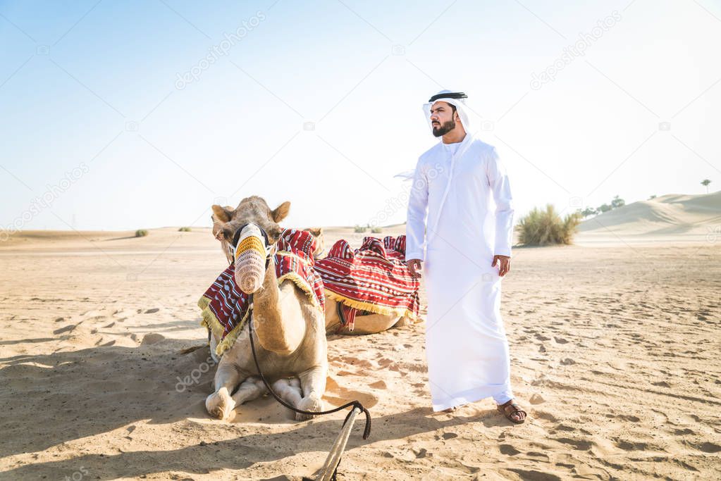 Handsome middle eastern man with kandura and gatra riding on a camel in the desert