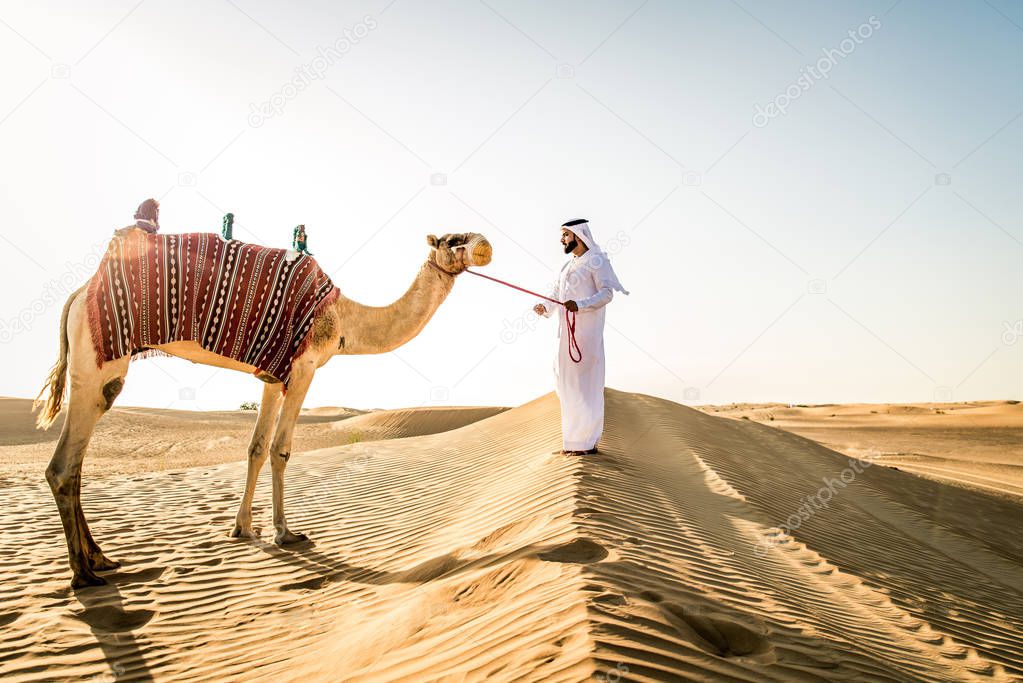 Handsome middle eastern man with kandura and gatra riding on a camel in the desert