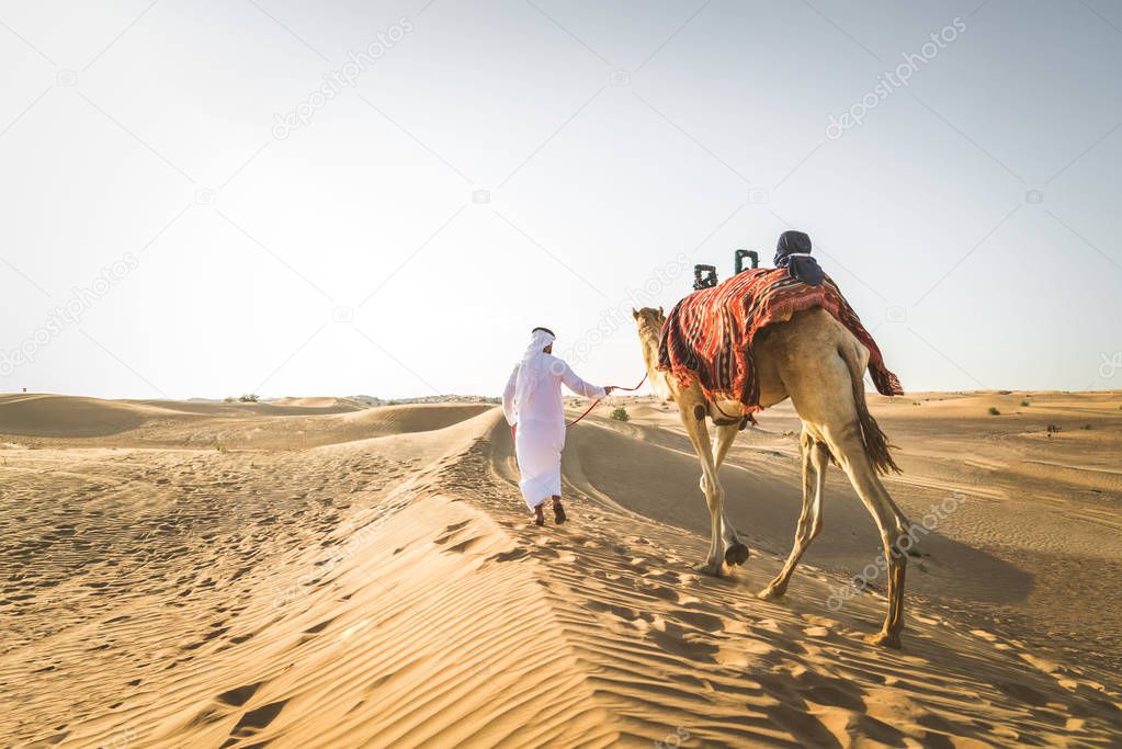 Handsome middle eastern man with kandura and gatra riding on a camel in the desert