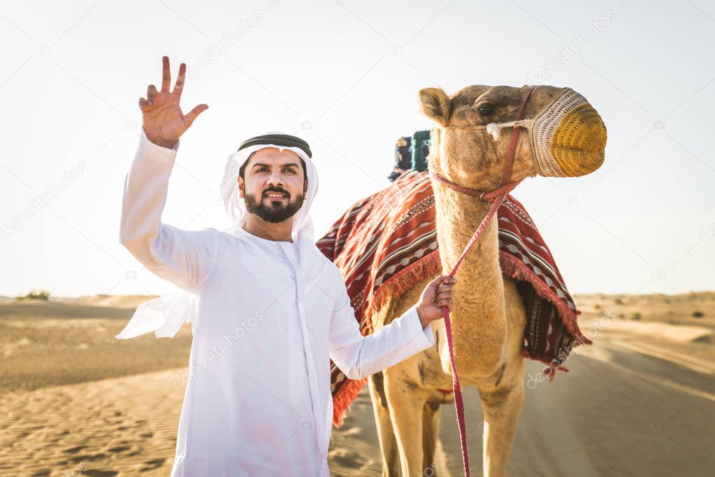 Handsome middle eastern man with kandura and gatra riding on a camel in the desert