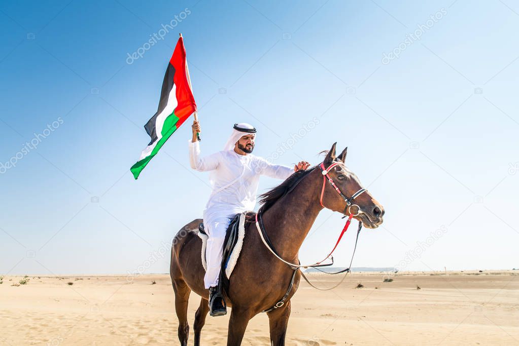 Middle eastern handsome man with typical emirates dress riding a arabic horse in the Dubai desert