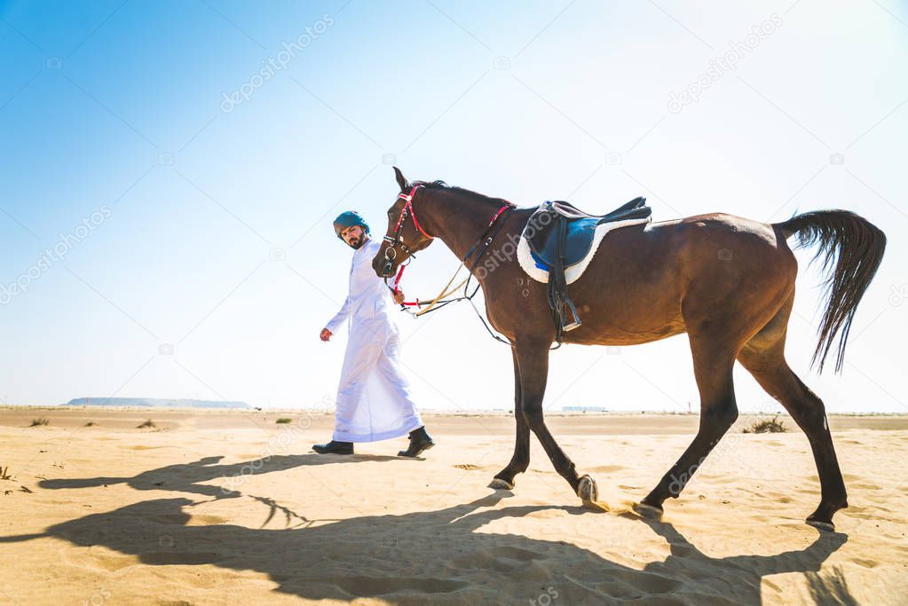 Middle eastern handsome man with typical emirates dress riding a arabic horse in the Dubai desert