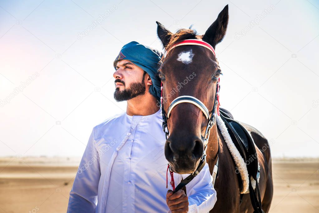 Middle eastern handsome man with typical emirates dress riding a arabic horse in the Dubai desert