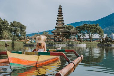 Pura Ulun Danu bir ahşap teknede genç kadın gezgin kürek çekmeye