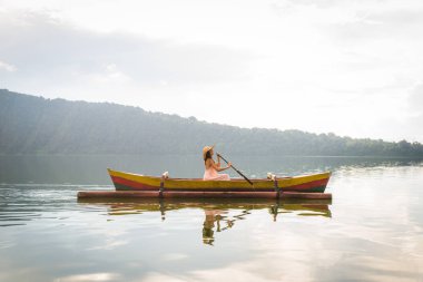 Pura Ulun Danu bir ahşap teknede genç kadın gezgin kürek çekmeye