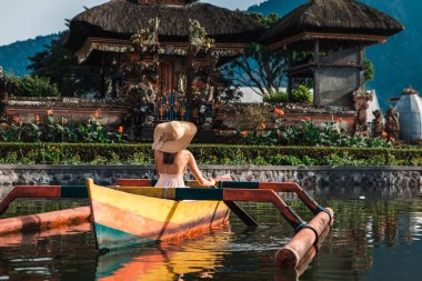 Pura Ulun Danu bir ahşap teknede genç kadın gezgin kürek çekmeye