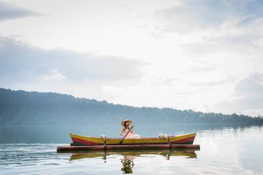 Pura Ulun Danu bir ahşap teknede genç kadın gezgin kürek çekmeye