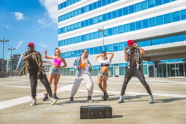 Hip hop ekibi dans ediyor, çok ırklı bir grup insan dışarıda eğleniyor.