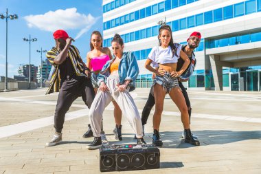 Hip hop ekibi dans ediyor, çok ırklı bir grup insan dışarıda eğleniyor.