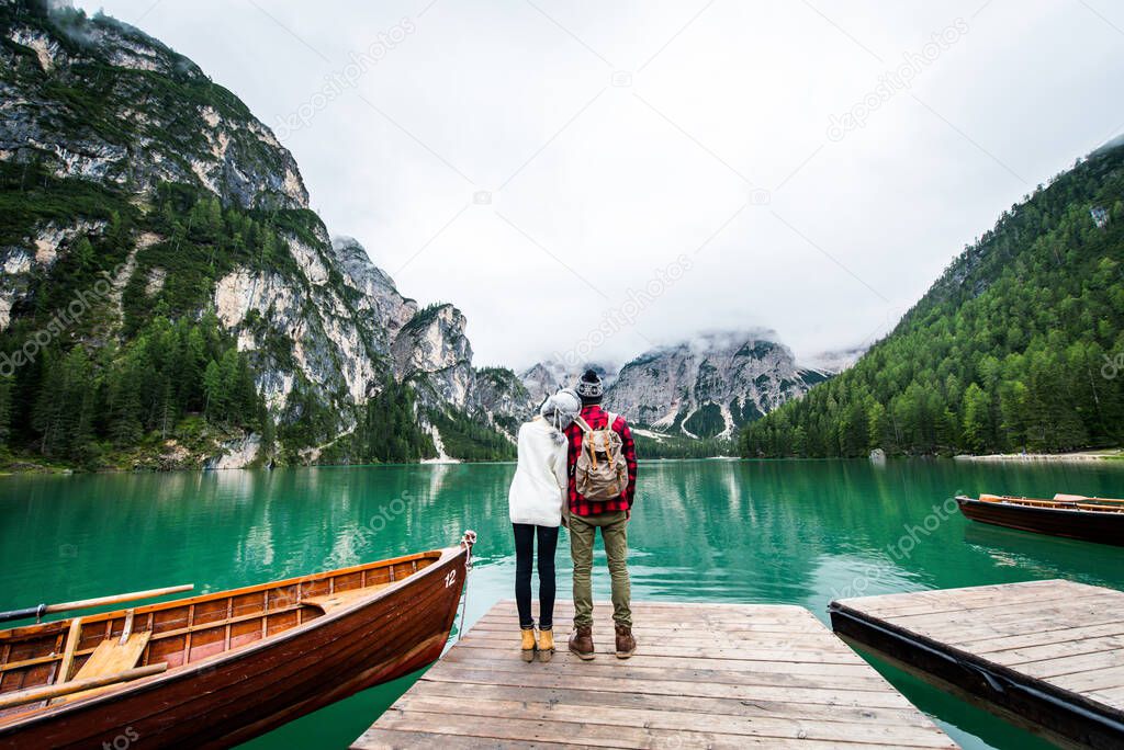Beautiful couple of young adults visiting an alpine lake at Braies, Italy - Tourists with hiking outfit having fun on vacation during autumn foliage - Concepts about travel, lifestyle and wanderlust