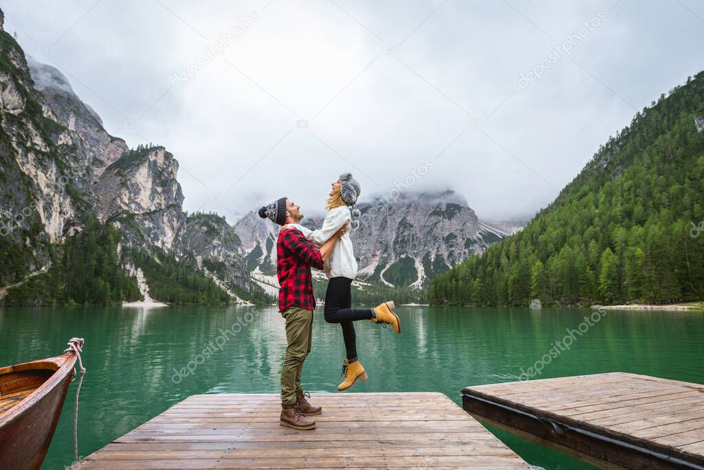 Beautiful couple of young adults visiting an alpine lake at Braies, Italy - Tourists with hiking outfit having fun on vacation during autumn foliage - Concepts about travel, lifestyle and wanderlust