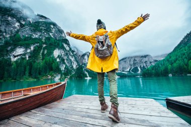 Dağ hikayeleri. Seyahat tutkusu tatilinde mutlu bir sırt çantası taşıyıcısı. Sarı yağmurluklu adam gölün önünde duruyor ve manzaranın tadını çıkarıyor.