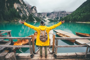 Dağ hikayeleri. Seyahat tutkusu tatilinde mutlu bir sırt çantası taşıyıcısı. Sarı yağmurluklu adam gölün önünde duruyor ve manzaranın tadını çıkarıyor.