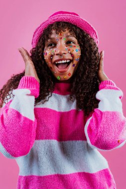 Pembe ve beyaz çizgili bir süveter, pembe güneş gözlüğü ve pembe bir şapka takan neşeli bir mankenin atölye çekimi.