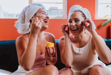 Havluya sarılmış, kozmetik ürünler ve göz bantları yapıştıran iki arkadaş, güzellik rutinlerini yaparken nefis bir kişisel bakım ve rahatlama anının tadını çıkarıyorlar.