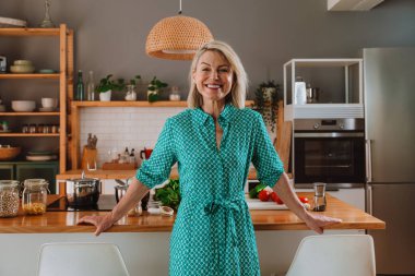 Modern mutfağında ayakta duran mutlu olgun bir kadın tezgahta çeşitli taze sebzelerle sağlıklı bir yemek hazırlamaya, sağlıklı bir yaşam tarzını desteklemeye hazır.