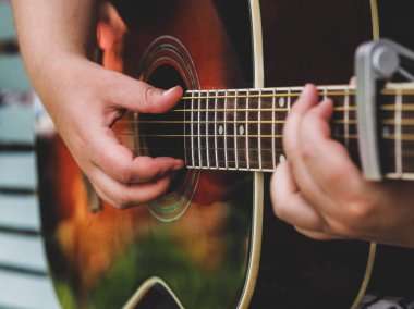 Akustik gitar çalınıyor. Boynu yakın, parmakları müzisyen.