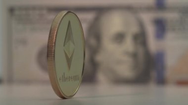 Altın sikke Etherium ETH beyaz yüzeyde döner. Arka planda Amerikan doları var. 100 dolarlık banknot. Makro görüntüler