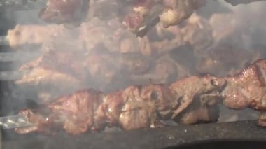 Aşçı ızgaradaki hafif kızarmış eti çevirir. Tatilde dışarıda barbekü şişi pişirmek.