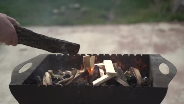 Avant le barbecue. L'homme met beaucoup de bois de chauffage dans un barbecue avec feu puis les redresse avec un bâton. Super ralenti 120 images FPS — Video