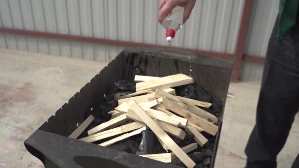 Campeggio. Preparare la legna da ardere prima di accendere un fuoco. Un uomo versa legna da ardere con del liquido per l'accensione. Giorno di ferie — Video Stock