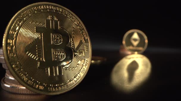 Gouden Bitcoin op de voorgrond en populaire digitale criptocoin Etherium op de achtergrond. Camera verschuiven focus van de ene munt naar de andere. Zwarte achtergrond. Handel in cryptomarkten — Stockvideo