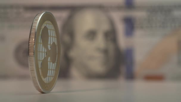 Срібна цифрова крипто-монета з золотим логотипом Ripple обертається на столі. Сто доларів США з обличчям Франкліна на задньому плані.. — стокове відео
